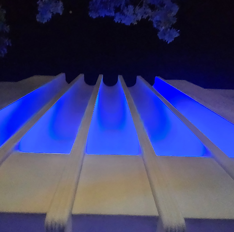 Blue Fins, a low-angle photograph by Mac Beach, captures cobalt-blue light illuminating the fluted white façade of a museum building in Lake Worth, Florida, against the night sky.