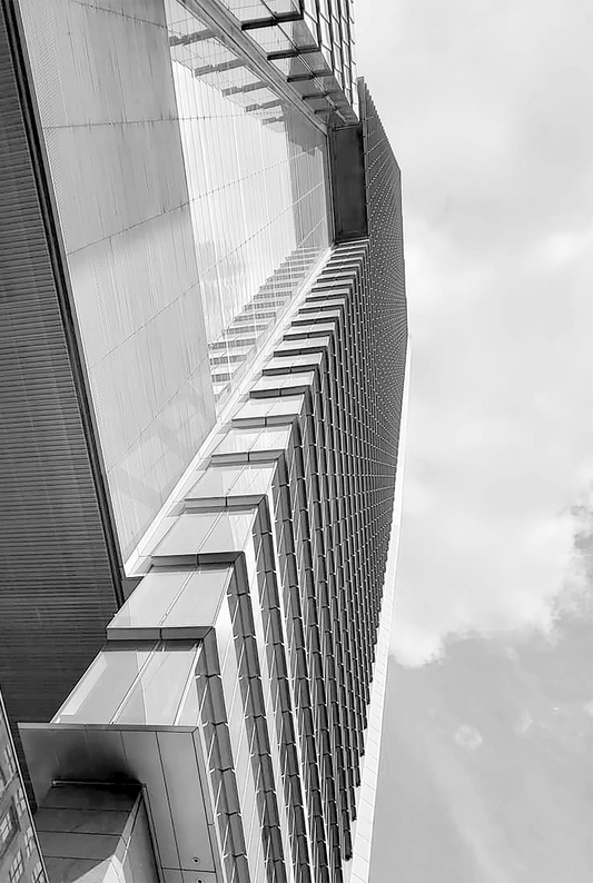Abstract work by Mac Beach capturing a low-angle black-and-white view of a glass high-rise façade, with repeating window fins and reflections extending toward a cloudy sky in Fort Lauderdale, Florida, 2022.