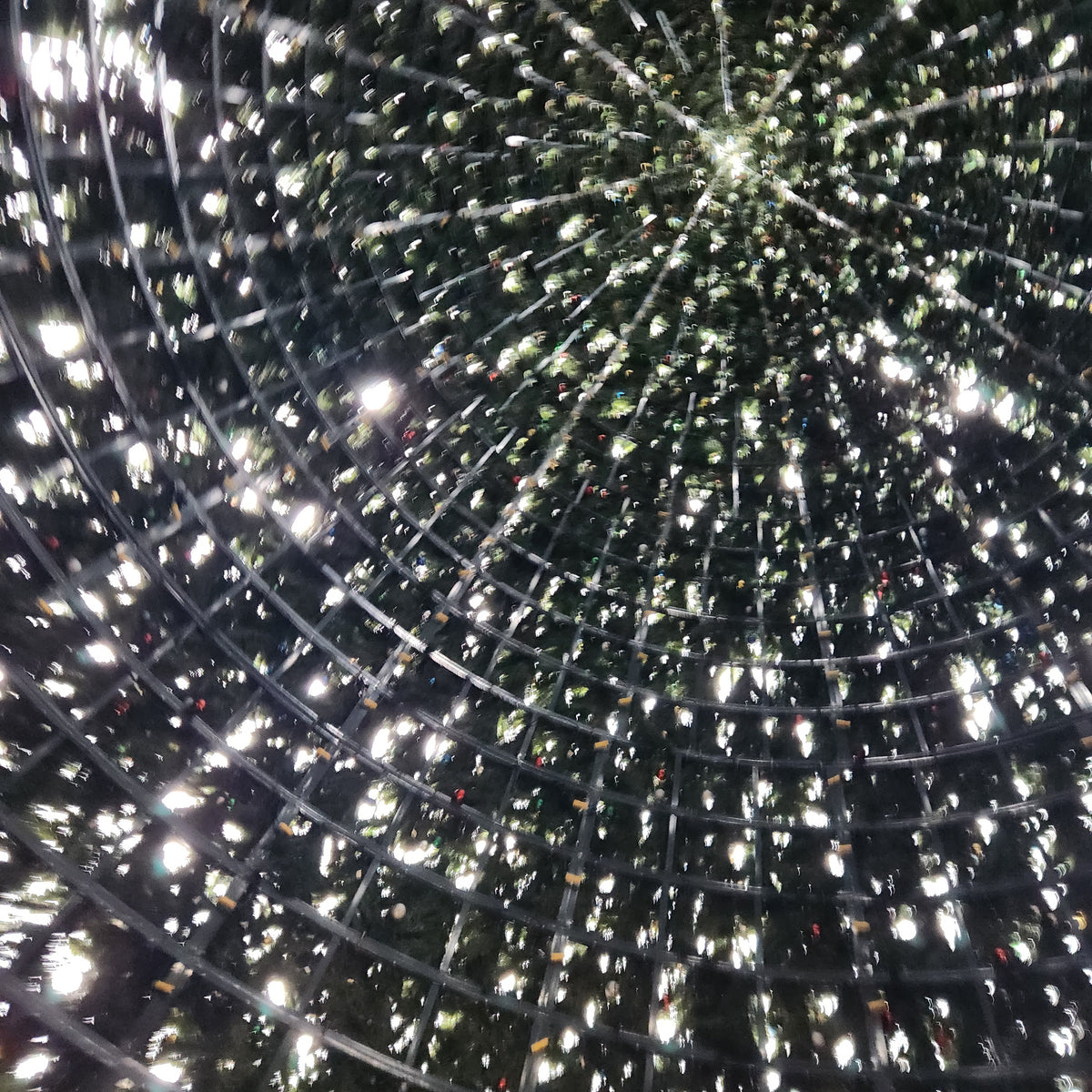 Abstract work by Mac Beach capturing an upward view through radiating metal framework, artificial evergreen branches, and star-like points of light inside Delray Beach’s annual Christmas tree, Florida, 2023.
