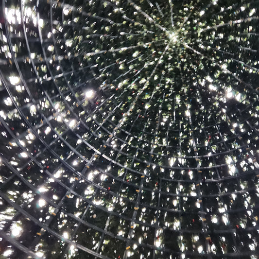 Abstract work by Mac Beach capturing an upward view through radiating metal framework, artificial evergreen branches, and star-like points of light inside Delray Beach’s annual Christmas tree, Florida, 2023.